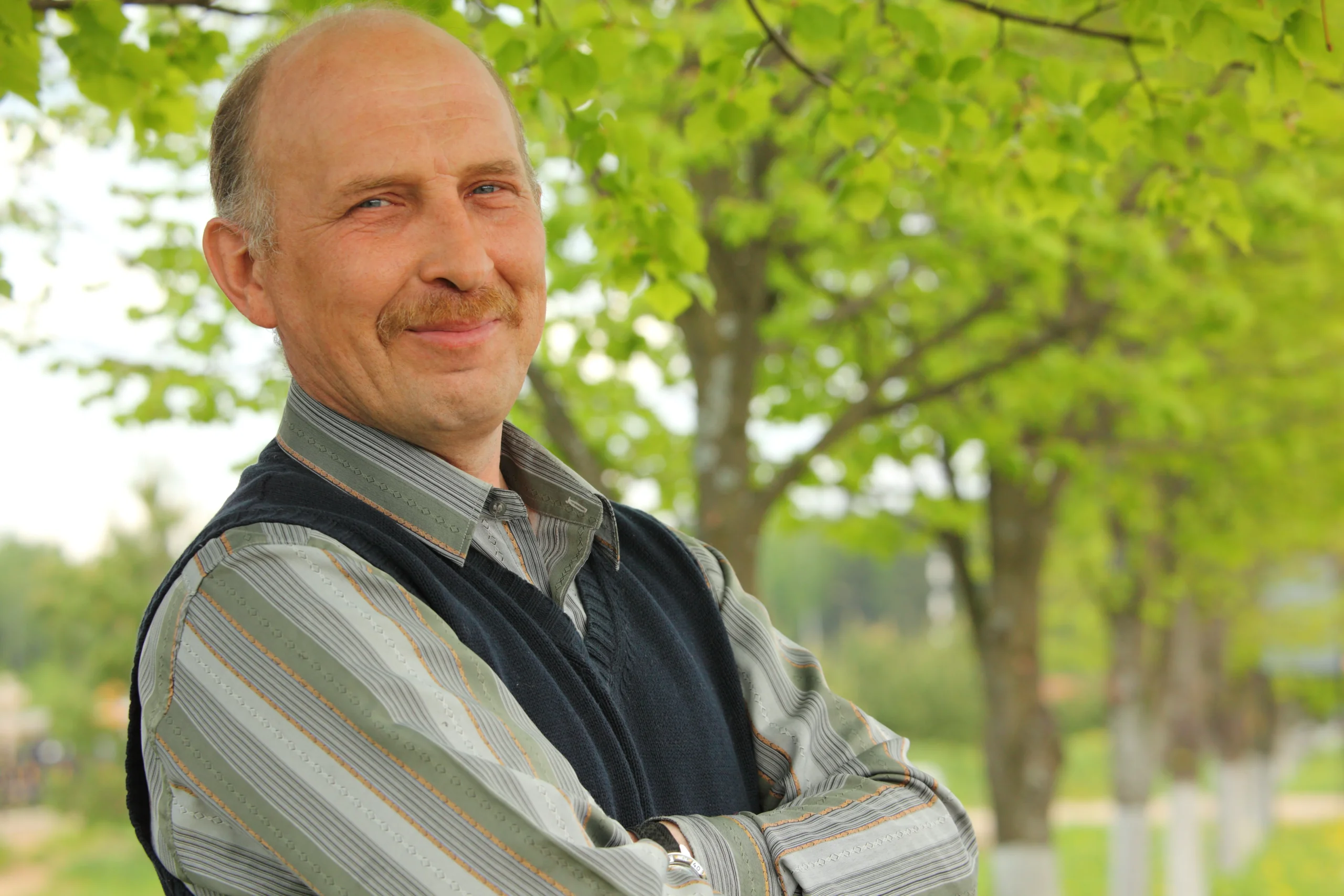 An older man outside smiling with his arms crossed.